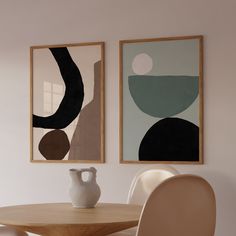 two paintings hang on the wall next to a table with chairs and a vase in front of it