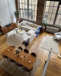 an aerial view of a living room and dining area with large windows, wood flooring, white couches, and wooden tables