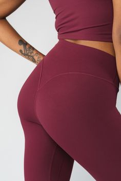 a woman in maroon leggings with tattoos on her arm and the bottom half of her body