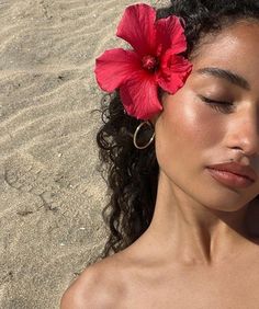 a woman laying on the beach with her eyes closed and a flower in her hair