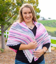 a woman wearing a crocheted shawl standing in front of a white fence