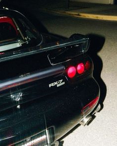 the rear end of a black car parked in a parking lot with its lights on