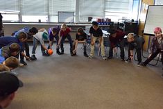 a group of young boys standing around each other in a circle playing with an orange ball