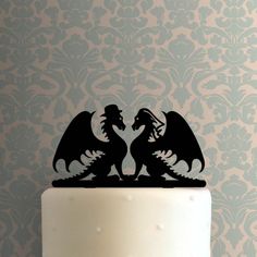 a cake topper with two black dragon silhouettes on it's side, in front of a blue damask wall