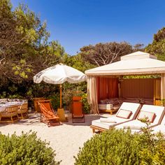 an outdoor cabana with lounge chairs and umbrellas on the sand in front of trees