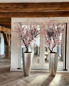 two vases with pink flowers in them sitting on a wooden floor next to a glass door