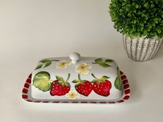 a white plate with strawberries on it next to a potted plant and vase