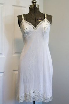 Gorgeous slip from the 1950s adorned with the most beautiful floral lace on the cups, hemline, and around the bust and top back. The hemline lace expands on the front to a larger triangular panel, adorned with the sweetest little embroidered white flowers with sage green leaves and stems. The bust cups have a three-flower lace panel with one embroidered flower in the centre. Adjustable straps with metal sliders. Falls approximately just below the knee (it's labelled "short", but keep in mind thi Lace Patchwork Fitted Slip Dress, Fitted Lace Slip Dress With Patchwork, Fitted Lace Patchwork Slip Dress, Fitted Cami Slip Dress With Delicate Lace, Fitted Slip Dress With Lace Trim For Wedding, Fitted Lace Trim Slip Dress For Wedding, White Slip Dress With Lace Trim And Spaghetti Straps, White Lace Slip Dress With Spaghetti Straps, White Wedding Camisole With Built-in Bra