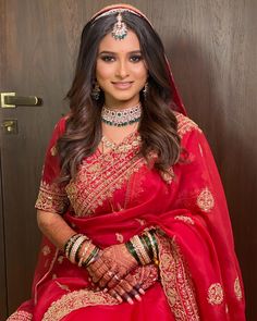 a woman in a red and gold bridal outfit posing for the camera with her hands on her hips