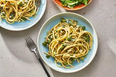 three plates of pasta and salad on a table with utensils next to them