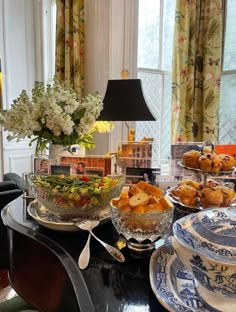 a table topped with plates and bowls filled with food next to a vase full of flowers