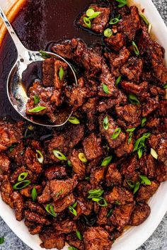 a bowl filled with meat and sauce on top of a table next to a spoon