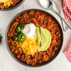 two bowls filled with chili, cheese and avocado on top of a table