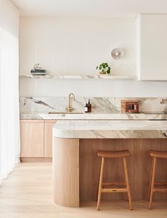 two wooden stools sit in front of a marble counter top and island with built - in shelving