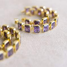 Limited Edition Add a touch of regal elegance to your style with our Gesuina Statement Hoop Earrings. Featuring twelve brilliant baguette-cut amethyst cubic zirconia stones, these hoops exude a captivating purple sparkle that elevates any look. Perfect for special occasions or adding a hint of glamour to your daily wear, these earrings are destined to be your go-to accessory for show-stopping sparkle and sophisticated charm. Details Medium-weight statement earrings Made of genuine cubic zirconia Luxury Multi-stone Hoop Earrings, Luxury Gemstone Hoop Earrings, Elegant Hoop Jewelry With Gemstone Accents, Elegant Gold Amethyst Hoop Earrings, Gold Elegant Hoop Earrings With Gemstone Accents, Elegant Gold Hoop Earrings With Gemstone Accents, Elegant Purple Hoop Earrings, Elegant Faceted Hoop Jewelry, Elegant Round Faceted Hoop Earrings