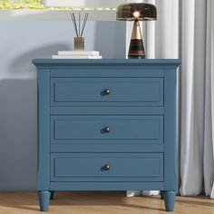 a blue chest of drawers with two lamps on top and a window in the background