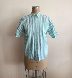 "Short-sleeved, teal and white striped, button-down shirt from the 1980s. Bust measures 20.5\" (52 cm) flat across and waist measures 19.5\" (49.5 cm) flat across. The shirt is 26\" (66 cm) long. Cotton. Original size is a medium." Classic Striped Short Sleeve Shirt For Spring, Fitted Vintage Short Sleeve Shirt For Spring, Retro Relaxed Fit Shirt For Daywear, Vintage Striped Summer Shirt, Retro Short Sleeve Shirt With Vertical Stripes, Vintage Striped Tops With Buttons, Vintage Striped Shirt With Buttons, Vintage Striped Cotton Shirt, Vintage Cotton Shirt With Striped Collar