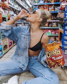 a woman is sitting on the floor eating food in a grocery store while looking at her cell phone