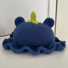 a crocheted blue hat with a green leaf on top sitting on a table