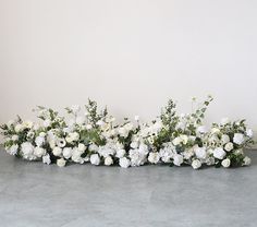 white flowers and greenery are arranged in a row on the floor next to a wall