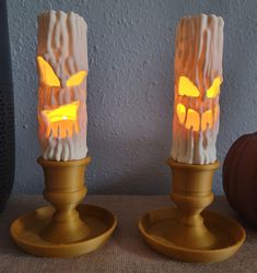 two candles with carved pumpkins on them sitting on a table next to each other