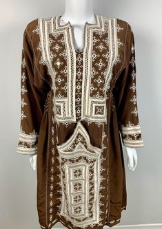 Our Vintage Brown Dress with White Embroidery is a stunning piece that seamlessly blends classic style with intricate details. Crafted with high-quality brown fabric, this dress features delicate hand embroidery in crisp white thread along the sleeves and hemline. The embroidery is done using traditional techniques, adding a touch of authenticity and uniqueness to the dress. The dress boasts a fitted bodice and a flowy skirt that flatters any body type. Perfect for any occasion, this dress can be dressed up with heels and statement jewelry, or dressed down with sandals for a more relaxed look. Overall, this Vintage Brown Dress with White Embroidery is a timeless piece that will elevate any wardrobe with its charm and sophistication. Please contact for measurements. Folk Style Long Sleeve Chikankari Dress, Folk Style Long Sleeve Embroidered Dress, Elegant Tunic Embroidered Dress With Floral Details, Elegant Floral Embroidered Tunic Dress, Traditional Beige Dress With Chikankari Embroidery, Traditional Beige Chikankari Embroidered Dress, Elegant Long Sleeve Cotton Embroidered Dress, Elegant Embroidered Brown Dress, Elegant Brown Embroidered Dress