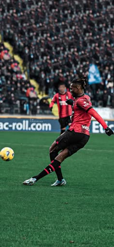 a man kicking a soccer ball on top of a field next to other people in the stands