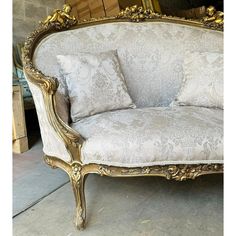 an ornate couch with gold trimming and pillows on it's back end, in front of a mirror