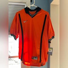 an orange nike soccer jersey hanging on a clothes hanger in front of a window