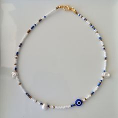 The Evil Eye is a luck charm believed to block the wearer from forms of bad luck that is willed onto by others. -This choker necklace is handmade with  a blue evil eye bead, a high quality, white irregular shaped freshwater pearl, blue,  gold and white coloured seed beads. - The necklace is about 14 inches long, however each necklace purchased comes with a chain extender ( 2 inches) so that you may adjust it to your desired length. - The seed beads are 2mm, the pearls are 8 x 6mm and the evil ey Evil Eye Choker, Colorful Choker, Seed Bead Choker, Necklace Evil Eye, Blue Choker, Polymer Clay Bracelet, Bead Choker, Clay Bracelet, Handmade Beaded Necklaces