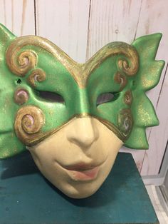 a green and gold mask sitting on top of a table