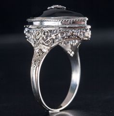 Vintage 1920's 14k White Gold Onyx Diamond Cocktail Style Ring .005ct 4.9gMetal Information: 14k White GoldTotal Weight: 4.9gBand Width: 1.8mmSize: 7.5Circa: 1920'sStone InformationMain StoneGem Type: OnyxShape: Marquise (18mm x 8mm)Color: BlackClarity/Quality: ANumber of Stones: 1Accent StonesGem Type: DiamondShape: Old Mine (1.0mm)Color: IClarity/Quality: SI1Carat Weight: .005ctNumber of Stones: 1Total estimated ctw (carat total weight): .005ctwEstimated Retail Price: $1875.00OUR PRICE: $1500.00SizingMany of our pieces can be re-sized at the buyers request. Please email us if you require our skilled professional services.46127 Hallmarked White Gold Domed Jewelry, Antique Engraved Ring With Polished Finish For Formal Occasions, Victorian Style Engraved Ring With Polished Finish, Victorian Style Formal Engraved Ring With Polished Finish, Victorian Black Enamel Rings For Anniversary, Victorian Black Enamel Anniversary Rings, Wedding Onyx Jewelry With Polished Finish, Evening Antique Jewelry With Polished Finish, Victorian Black Enamel Wedding Rings