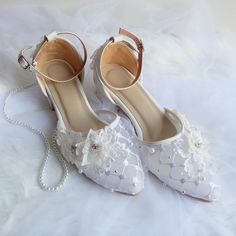 a pair of white wedding shoes with flowers and pearls on the heel, sitting on a bed