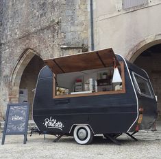 an old camper parked in front of a building with a chalkboard sign next to it