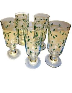 six glasses are lined up on a white tablecloth with green shamrocks all over them