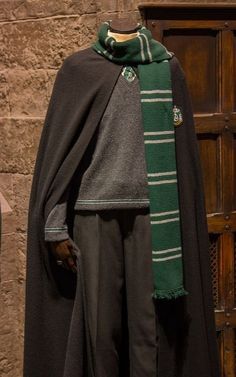 a mannequin wearing a green scarf and coat in front of a wooden door