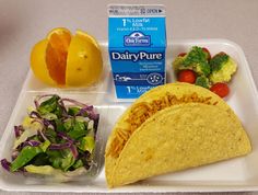 a tray with some tacos, salad and oranges on it next to a carton of dairy pure