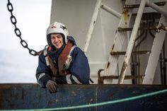 a man wearing a helmet leaning on the side of a boat with chains hanging from it