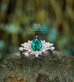 a ring with a green stone surrounded by white diamonds on top of a mossy rock