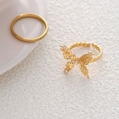 ✦ Indulge in the elegance of our Chunky 18K Gold Butterfly Cocktail Ring made with molten design and 18k gold plating. Perfect for any occasion, this statement ring features a bold butterfly design, adjustable fit, and serves as a luxurious gift for friends. Elevate your style with this exclusive piece that exudes sophistication and uniqueness. ----------- DETAILS ----------- - Color: Gold - Ring Size: 17.3mm (Approximately to Size US7) - Width: 1.8cm - Materials: 18K Gold Plated, Cubic Zirconia Elegant Adjustable Gold Butterfly Ring, Adjustable Gold Butterfly Open Ring, Adjustable Gold Butterfly Ring, Adjustable Yellow Gold Butterfly Ring, Adjustable Gold Butterfly Ring For Anniversary, Gold Butterfly Ring For Wedding, Cocktail Rings Statement, Butterfly Cocktail, Elegant Gothic