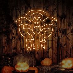 a neon sign that says halloween with pumpkins in front of it and a bat on top