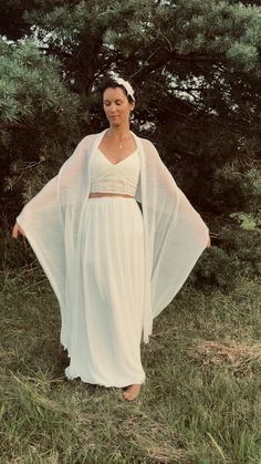 a woman wearing a white dress and cape standing in the grass