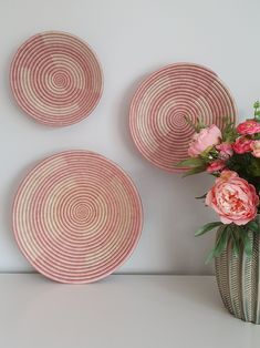 three pink and white plates sitting on top of a table next to a vase with flowers