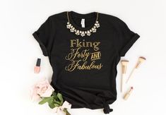 a black t - shirt with gold lettering on it next to some flowers and lipstick