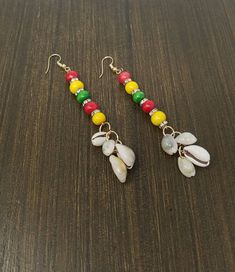 two pairs of earrings with colorful beads and charms on them sitting on a wooden surface