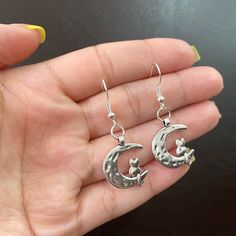 A pair of statement moon earrings has the power to elevate your everyday look. This unique cat and moon earring design looks gorgeous paired with any casual or dressy outfit.  ● 17.3mm 925 sterling silver fish hook  ● 20mm alloy moon charm  ● Made with hypoallergenic material * Please note for health and safety purposes and quality control these earrings are final sale Please DM me with any questions. ABOUT ABBYANDCO JEWELRY✨ 💖All abbyandco pieces are made with hypoallergenic gold plated and st Whimsical Moon Charm Earrings Gift, Whimsical Silver Hypoallergenic Earrings, Whimsical Silver Metal Earrings, Silver Cat Design Dangle Earrings, Cat And Moon, Moon Earring, Dressy Outfit, Celestial Earrings, Silver Fish