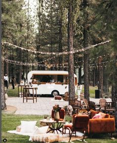 an rv parked in the middle of a forest with lots of furniture and lights strung across it