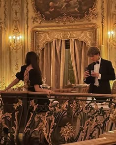 a man and woman standing on a balcony looking at their cell phones in front of them