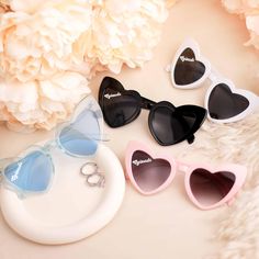 three pairs of heart shaped sunglasses sitting on top of a white plate next to flowers