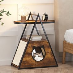 a cat in a wooden triangle shaped shelf next to a bed and nightstand with books on it